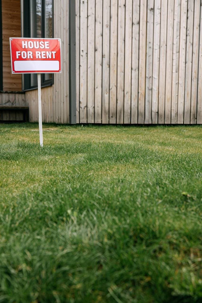 A red-and-white "for rent" sign on a residential front lawn.